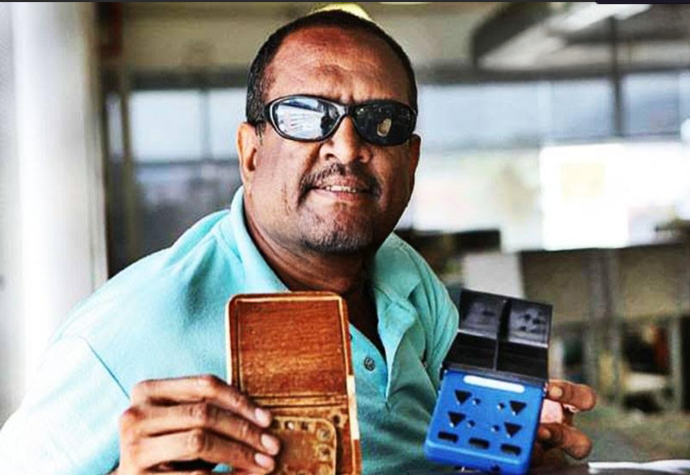 Foto de Alfredo Lápiz sosteniendo 2 dispositivos tiflotecnológico lápiz y cuaderno electrónico y pimpert 4B